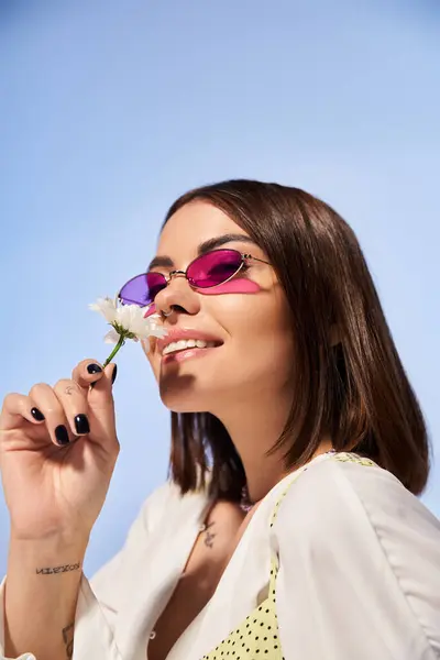 A stylish young woman with brunette hair wearing sunglasses, holding a vibrant flower. — Stock Photo