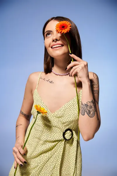 Eine gelassene junge Frau mit brünetten Haaren in einem leuchtend gelben Kleid hält anmutig eine zarte Blume in der Hand. — Stockfoto