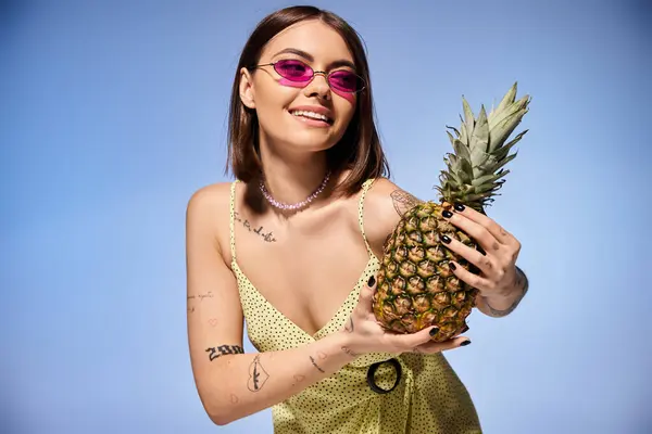 A young woman in a yellow dress gracefully holds a pineapple in a studio setting. — Stock Photo