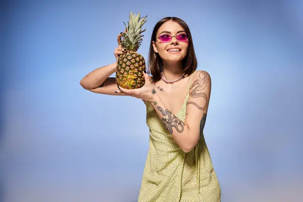 Una giovane donna dai capelli castani posa elegantemente in un abito giallo vibrante, con in mano un ananas fresco. — Foto stock