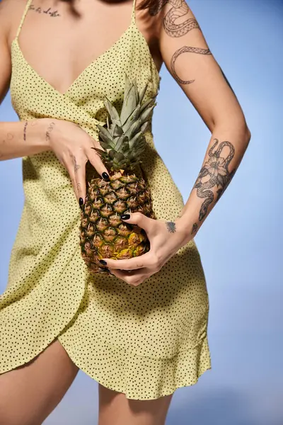 A young woman with brunette hair stands elegantly in a yellow dress, holding a fresh pineapple. — Stock Photo