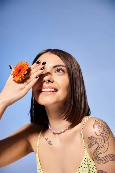 Une jeune femme aux cheveux bruns tient délicatement une fleur en fleurs dans un cadre de studio serein. — Photo de stock