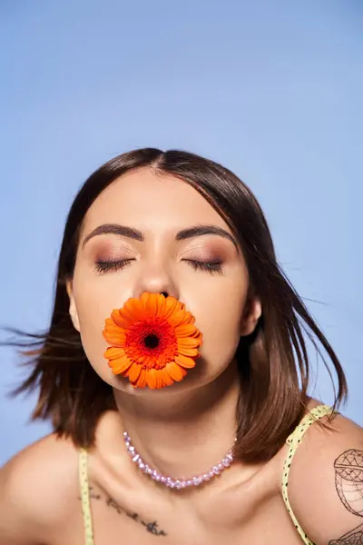 Une jeune femme aux cheveux bruns tient captivante une fleur dans sa bouche, mettant en valeur l'élégance et le lien avec la nature. — Photo de stock
