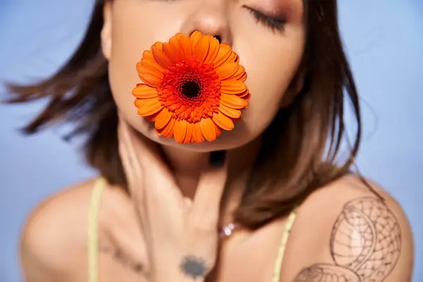 A young woman with brunette hair delicately holds a vibrant flower in her mouth, exuding elegance and grace. — Stock Photo