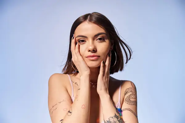 Una joven con el pelo moreno muestra orgullosamente un tatuaje en su brazo mientras posa en un estudio. - foto de stock