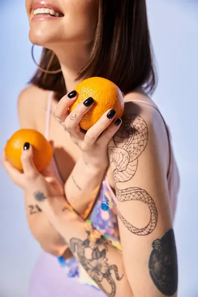 Una giovane donna con i capelli castani tiene con grazia due arance tra le mani in un ambiente da studio. — Foto stock