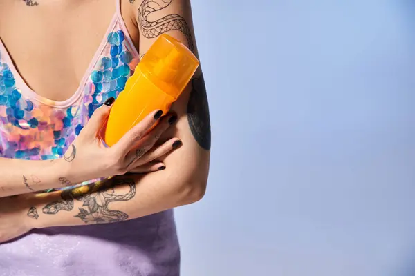 Una joven con tatuajes, cabello moreno, sosteniendo un protector solar amarillo en un ambiente de estudio. - foto de stock