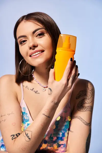 Una mujer morena con tatuajes sosteniendo una botella de protector solar. - foto de stock