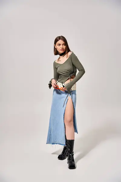 A young woman with brunette hair poses stylishly in a skirt and boots in a studio setting. — Stock Photo