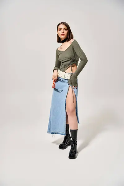 Une jeune femme aux cheveux bruns sourit en posant dans une jupe et des bottes en studio. — Photo de stock