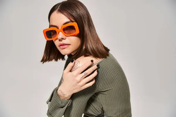 Eine junge brünette Frau posiert in leuchtend grünem Pullover und orangefarbener Sonnenbrille in einem Studio-Setting. — Stockfoto