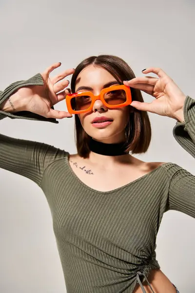 Eine stylische junge Frau mit brünetten Haaren trägt ein grünes Hemd und eine orangefarbene Sonnenbrille in einem Studio-Setting. — Stockfoto