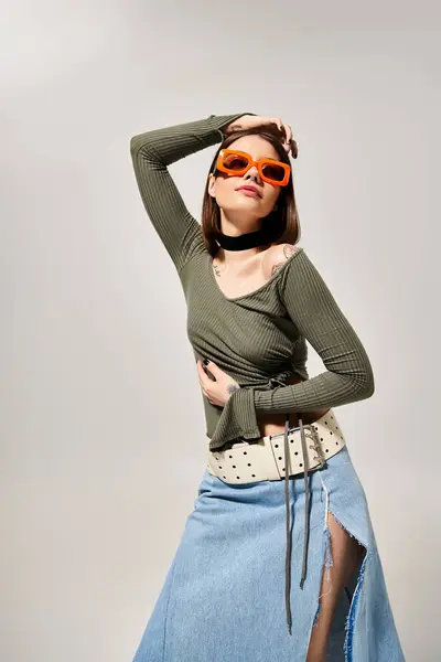 Una donna bruna che indossa una gonna e occhiali da sole posa con fiducia per una foto in un ambiente da studio. — Foto stock