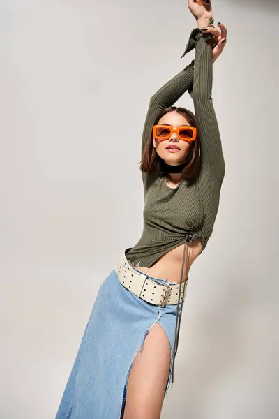 A chic brunette woman strikes a pose in a stylish skirt and sunglasses, exuding confidence and elegance in a studio setting. — Stock Photo