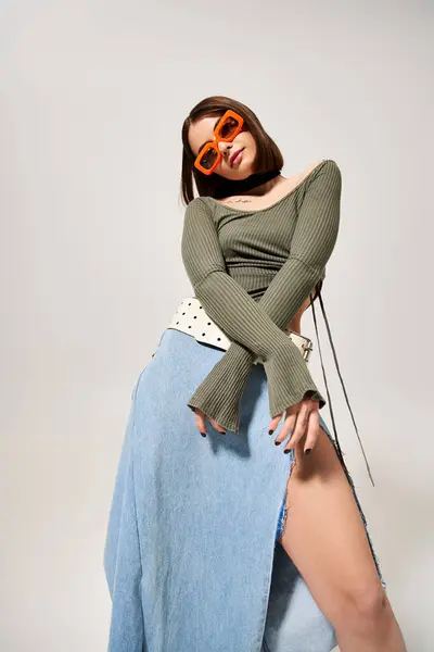 A young woman with brunette hair strikes a stylish pose in a studio while wearing a skirt and sunglasses. — Stock Photo