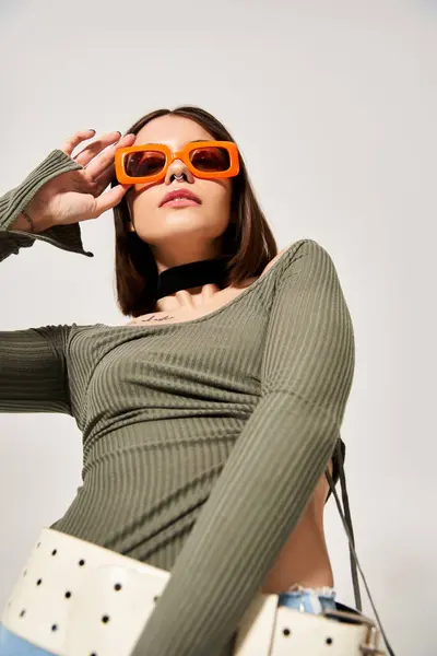 Eine junge Frau mit brünetten Haaren posiert in einem Studio-Setting mit einem leuchtend grünen Oberteil und trendiger orangefarbener Sonnenbrille. — Stockfoto