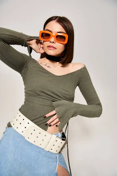 Una giovane donna elegante con capelli castani che indossa un top verde e occhiali da sole arancioni in un ambiente da studio. — Foto stock
