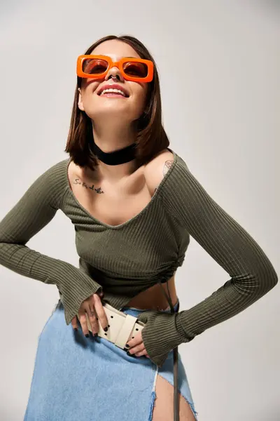 A fashionable young brunette woman confidently wears sunglasses and a stylish skirt in a studio setting. — Stock Photo