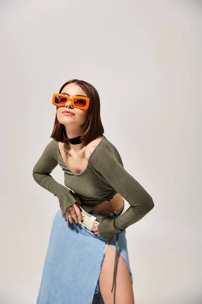 Una giovane donna bruna elegante posa fiduciosa in una gonna e occhiali da sole per una fotografia. — Foto stock