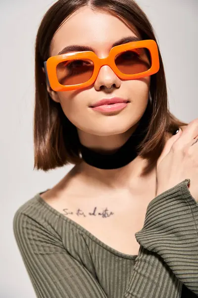 Uma mulher morena transpira estilo e confiança enquanto usa óculos de sol laranja na moda em um ambiente de estúdio. — Fotografia de Stock