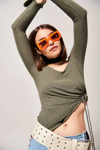 Una giovane donna con capelli castani che colpisce una posa in una camicia verde e occhiali da sole arancioni. — Foto stock