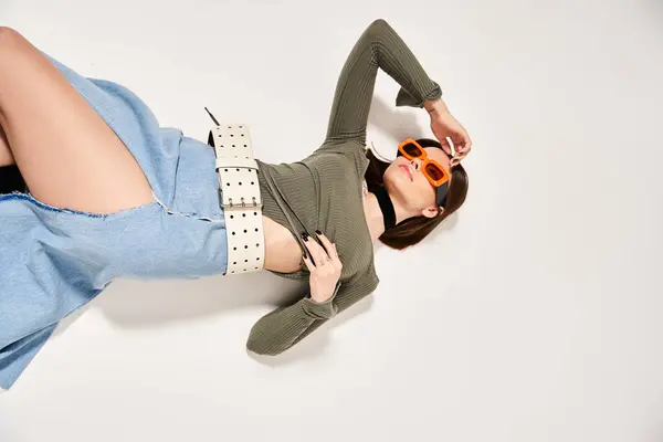 Une jeune femme aux cheveux bruns couchés sur le sol, portant des lunettes de soleil en studio, respirant un sentiment de calme et de détente. — Photo de stock