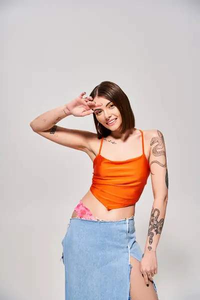 Une jeune femme aux cheveux bruns pose en toute confiance dans un studio portant un haut orange et une jupe bleue fluide. — Photo de stock