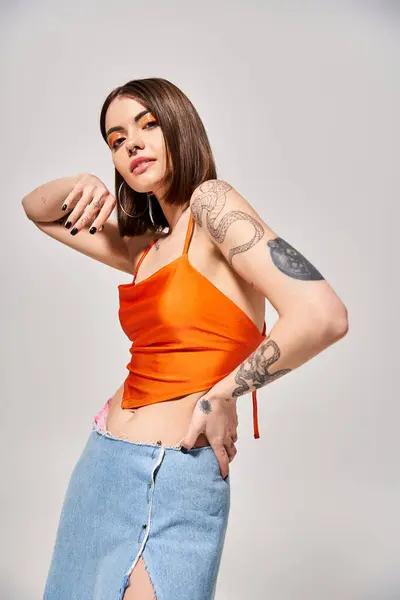 Une jeune femme aux cheveux bruns pose en toute confiance dans un décor studio tout en portant un haut orange. — Photo de stock