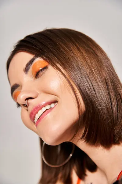 Una mujer joven con el pelo moreno lleva unos sorprendentes delineadores de ojos naranjas y negras en su cara en un ambiente de estudio. - foto de stock