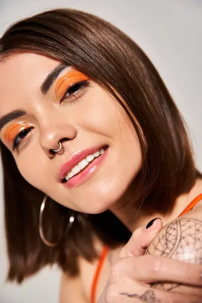 A young woman with brunette hair wearing bold orange makeup gazes fiercely — Stock Photo