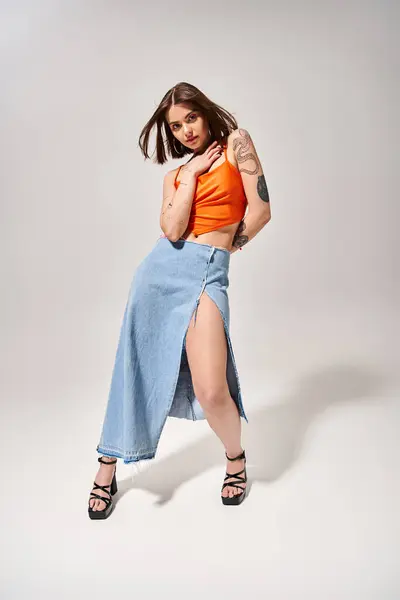 Eine junge Frau mit brünetten Haaren posiert in einem Studio und trägt ein orangefarbenes Oberteil und einen blauen Rock, der Eleganz und Anmut ausstrahlt. — Stockfoto