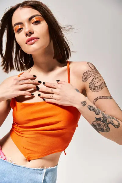 A young woman with brunette hair showcasing intricate tattoos on her arms and chest in a studio setting. — Stock Photo