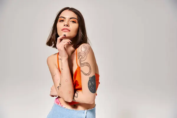 Una joven con el pelo morena y tatuajes toma una pose en un estudio para una foto. - foto de stock