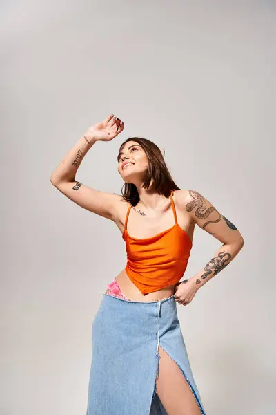 A young woman with brunette hair wearing an orange top and blue skirt twirls in a vibrant studio setting. — Stock Photo