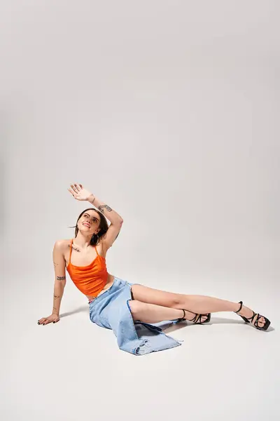 Eine junge Frau mit brünetten Haaren in einem orangefarbenen Oberteil liegt friedlich auf dem Boden in einem Studio-Setting. — Stockfoto