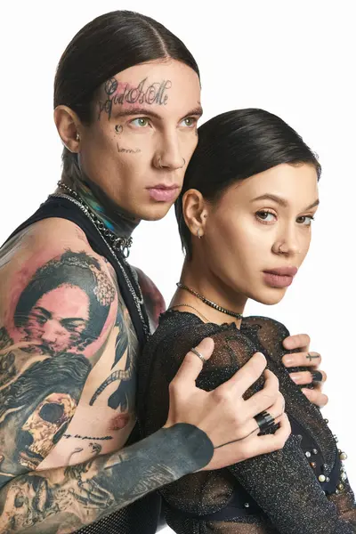 Un jeune homme et une jeune femme avec des tatouages élégants sur les bras posent en toute confiance dans un studio sur un fond gris. — Photo de stock
