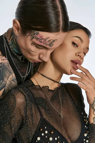 Hombre con tatuajes faciales atrevidos posando en un estudio con mujer sobre un fondo gris. - foto de stock