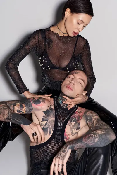 Une jeune femme s'assoit gracieusement sur le dos d'un homme dans un studio, les deux mettant en vedette des tatouages, sur fond gris. — Photo de stock