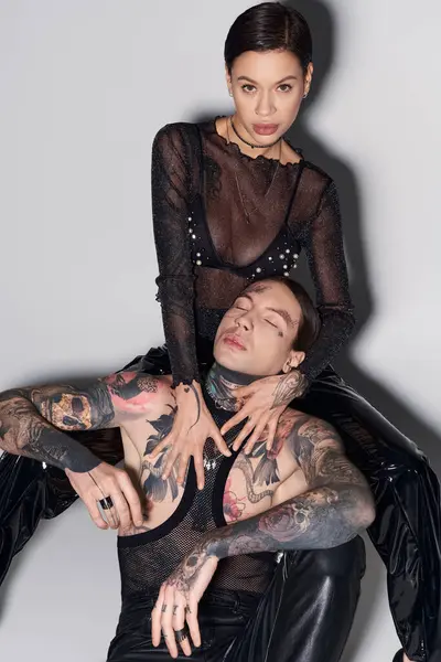 A woman with tattoos sits gracefully on the back of a man in a serene studio setting on a grey background. — Stock Photo
