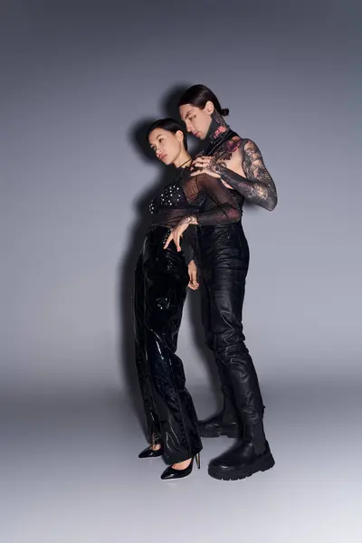 A young tattooed couple posing gracefully in a studio against a grey background. — Stock Photo