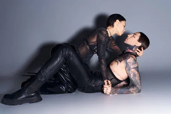 A young tattooed couple relaxing together on a grey backdrop in a serene and intimate embrace. — Stock Photo