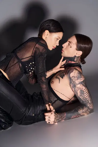 Une femme tatouée se trouve à côté d'un homme dans un studio sur fond gris, se connectant dans un moment d'intimité. — Photo de stock
