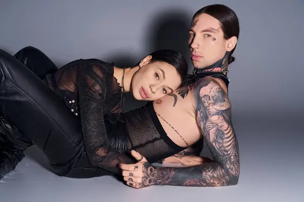 A young tattooed couple strikes a pose in a studio against a grey backdrop. — Stock Photo
