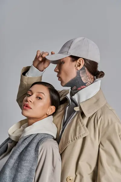 Ein junger Mann und eine junge Frau im Trenchcoat stehen nebeneinander in einem Atelier vor grauem Hintergrund. — Stock Photo