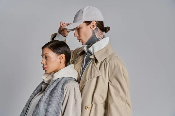 A young man and woman stand stylishly in trench coats, exuding elegance and unity on a grey studio background. — Stock Photo