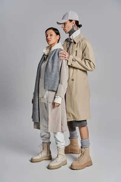 A young man and woman in stylish trench coats standing closely together in a studio on a grey background. — Stock Photo