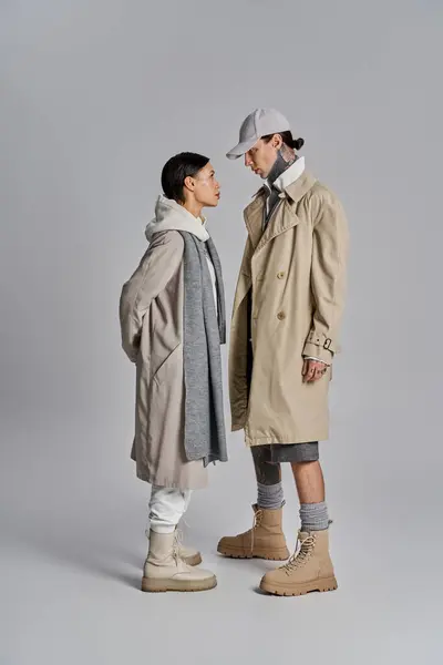 Couple stand side by side in stylish trench coats, exuding a sophisticated and fashionable vibe against a grey backdrop. — Stock Photo