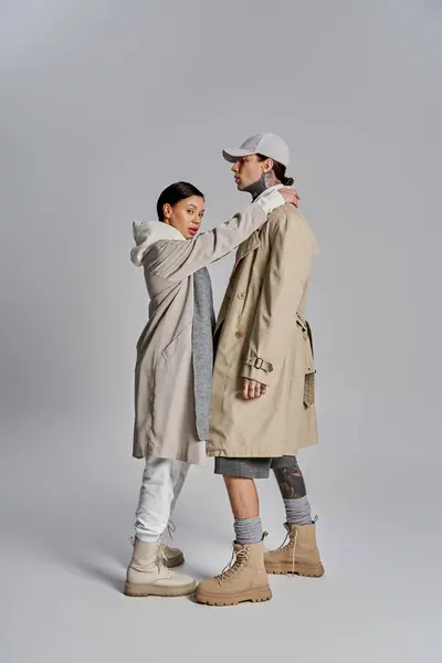 A young stylish couple in trench coats stands gracefully together in a studio against a grey background. — Stock Photo