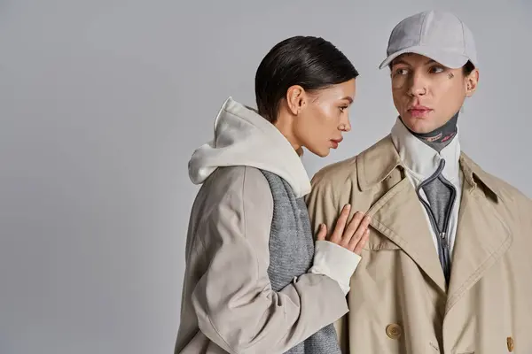 A young man and woman wearing trench coats stand next to each other in a studio against a grey background. — Stock Photo