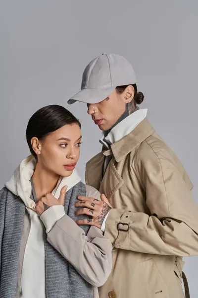 A young stylish couple in trench coats stands next to each other in a studio against a grey background. — Stock Photo